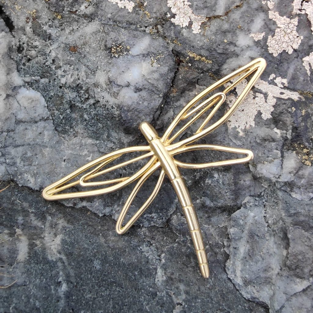 A dragon fly broach/pendant made in gold, photographed against a grey rock